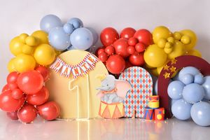 Colorful balloon arch with yellow, blue, and coral balloons decorating a first birthday party setup with circus theme elements.