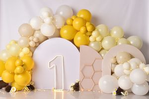 Modern first birthday backdrop with yellow and cream balloon garland and geometric accents.