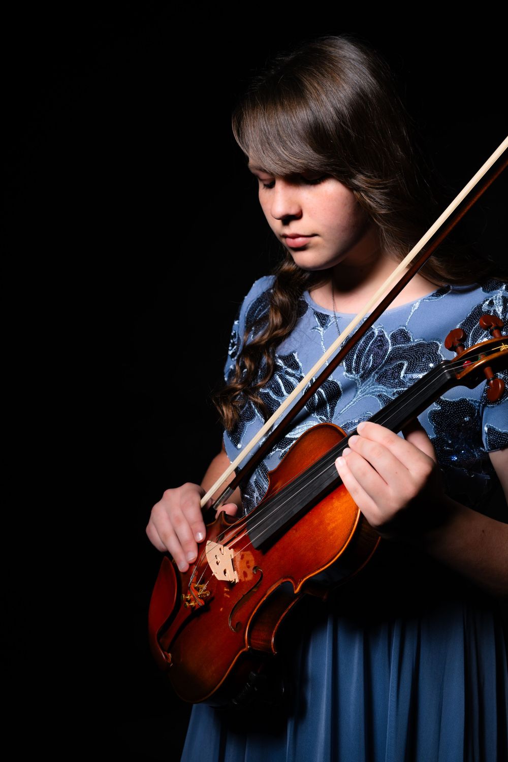 Violinist in flowing blue dress performs against black backdrop.