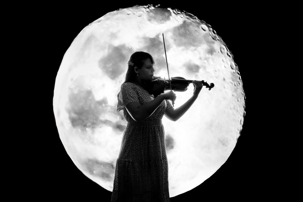Silhouetted musician performs against large glowing moon backdrop.