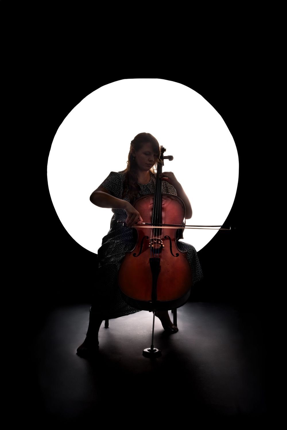 Dramatic silhouette of musician playing cello against circular white backdrop.
