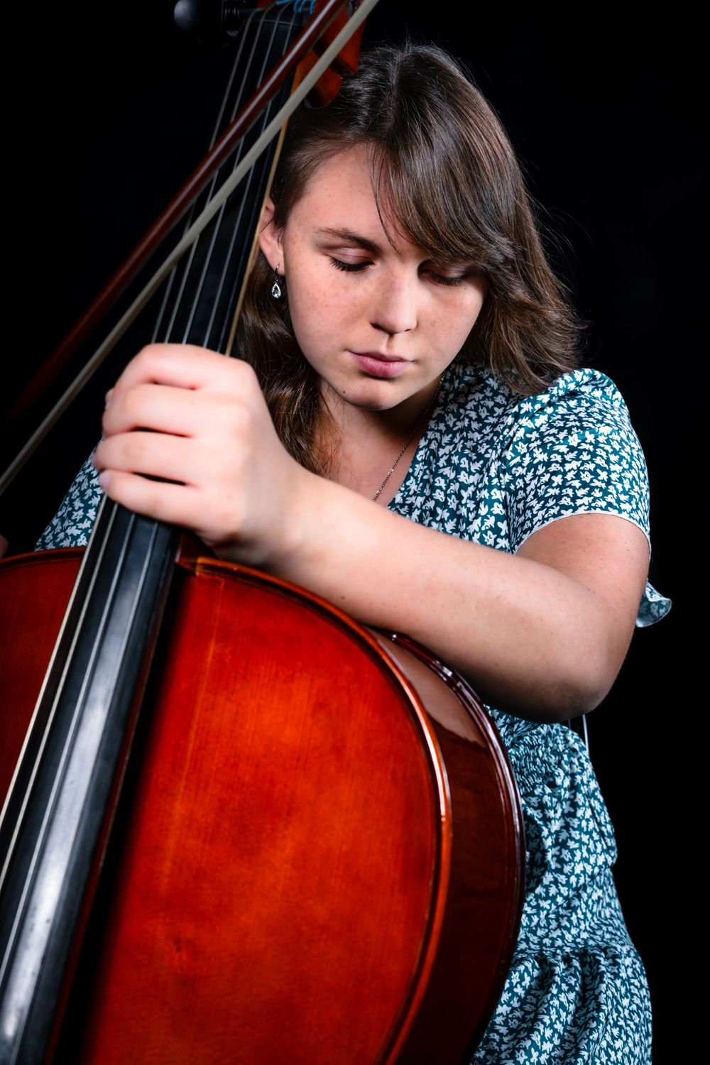 Close-up shots of cellist performing with wooden instrument against black backdrop.