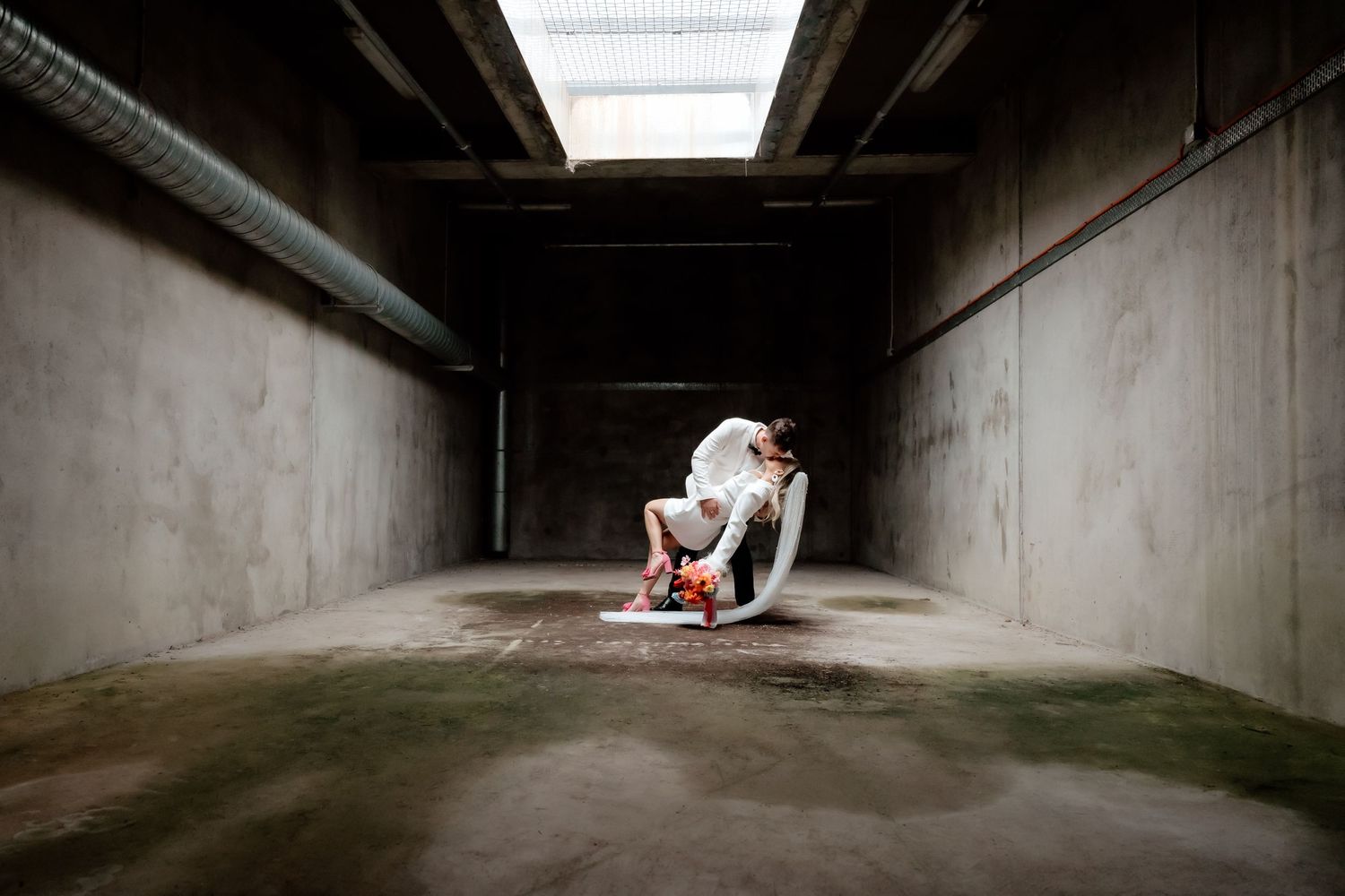 Artistic wedding photo in an industrial concrete tunnel with dramatic lighting.