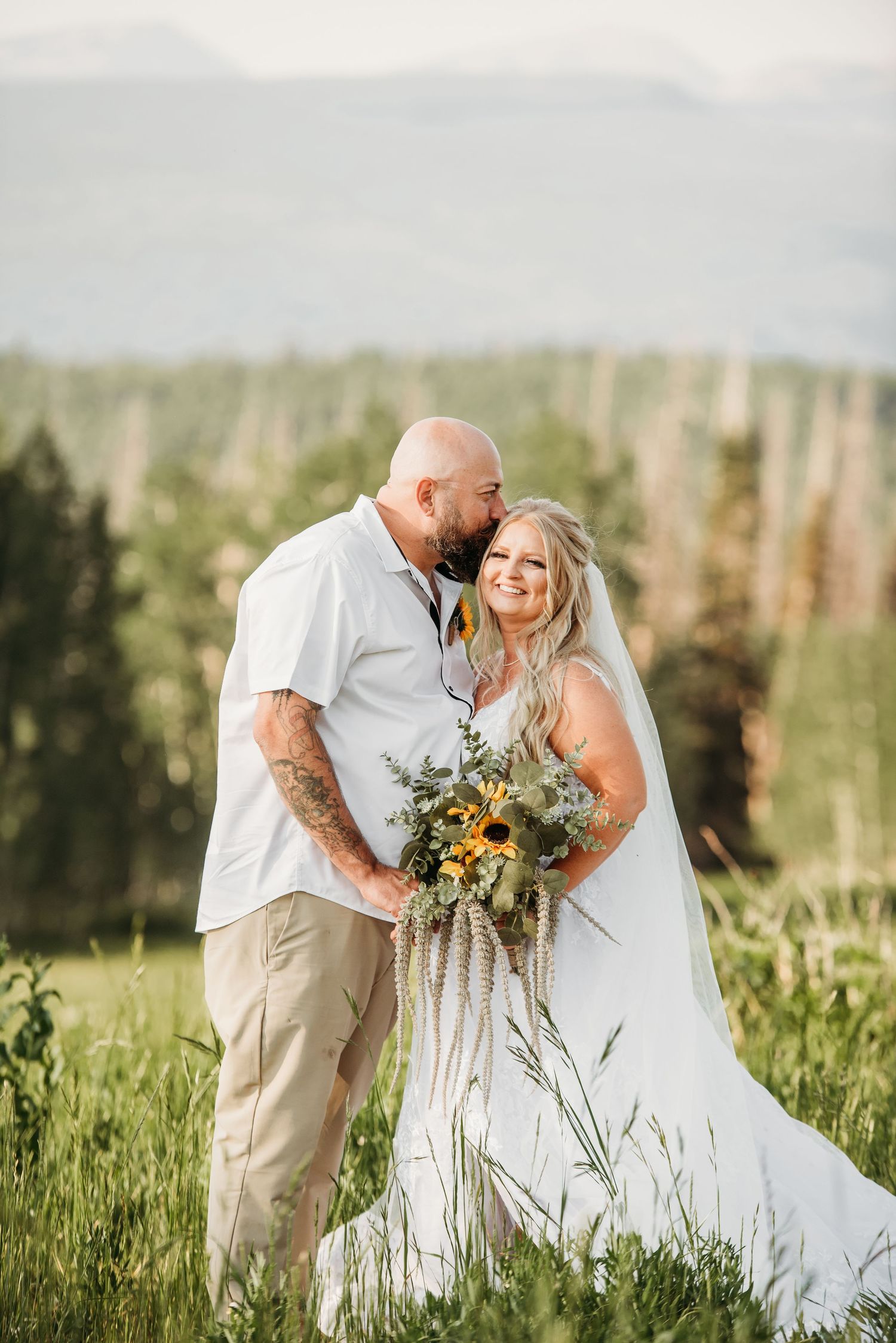 Newlyweds share an intimate moment in a mountain meadow with sunlit backdrop.