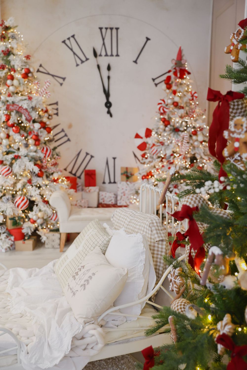 Elegant Christmas decor with white trees, clock, and red accents against a cozy armchair setting.