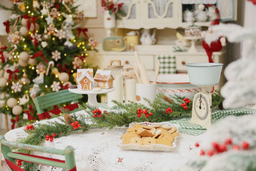 Christmas kitchen scene with decorated tree, cookies on plate, and evergreen garland with red berries.