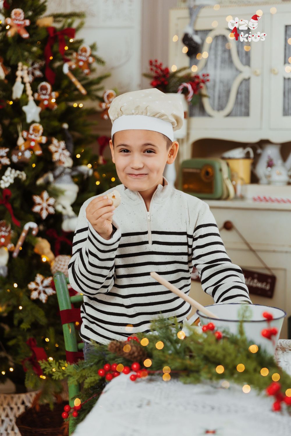 Child in striped shirt and chef hat baking Christmas treats in festive kitchen setting.