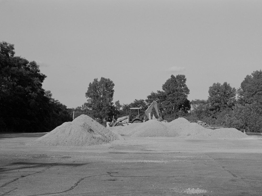 Monochromatic sequence showing seven stages of a dirt jump ramp being constructed at a bike park.