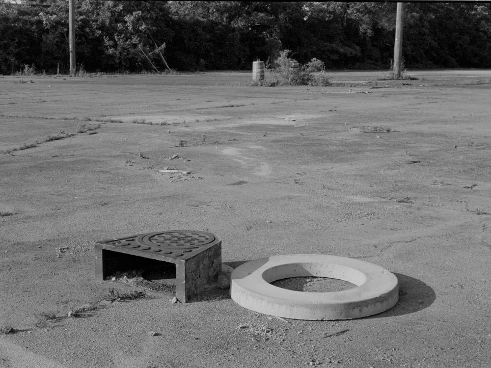 Black and white image of two storm drain covers on a cracked concrete surface in an empty lot.