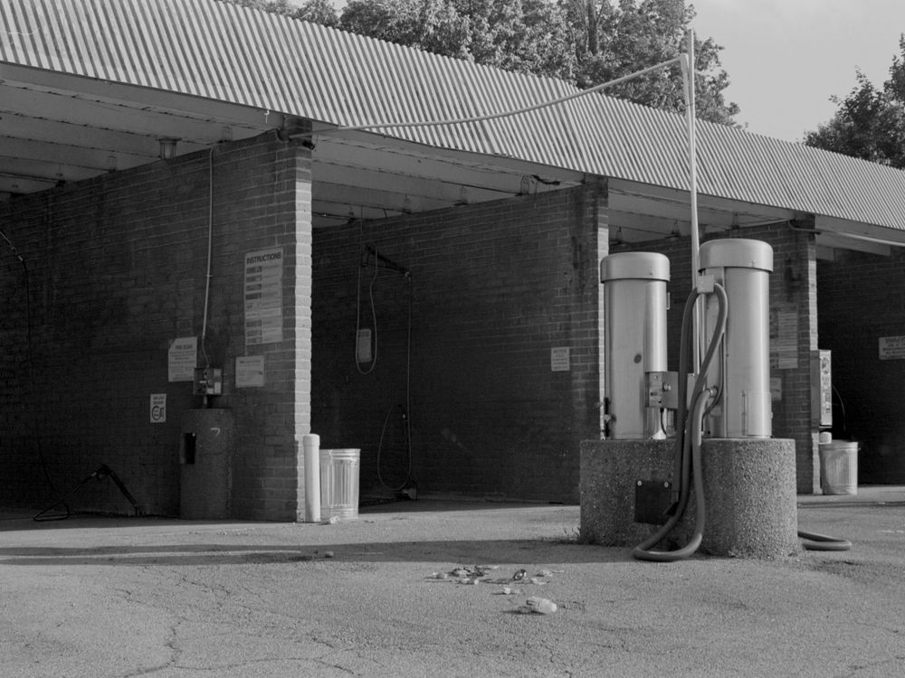 Vintage gas station with metal roof and classic fuel pumps under covered area in black and white photo.