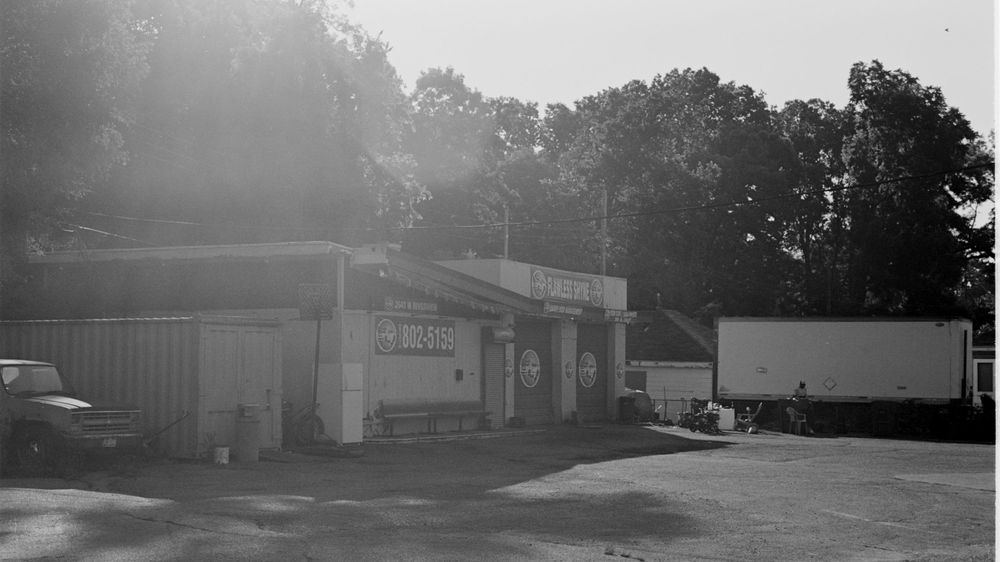 Small vintage gas station and garage with pickup truck parked outside in black and white photograph.