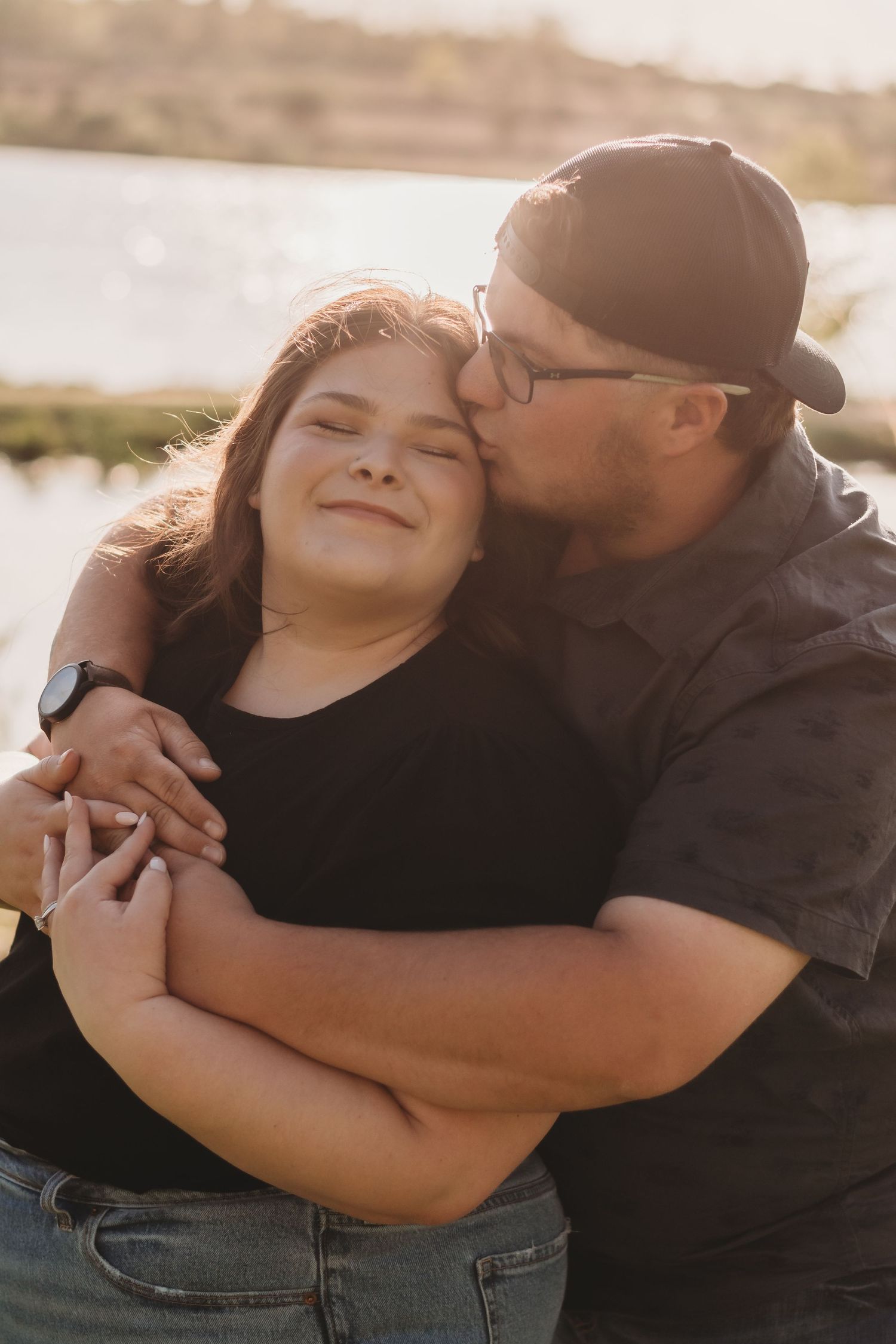 A tender embrace shared between two people against a sunlit backdrop by the water.