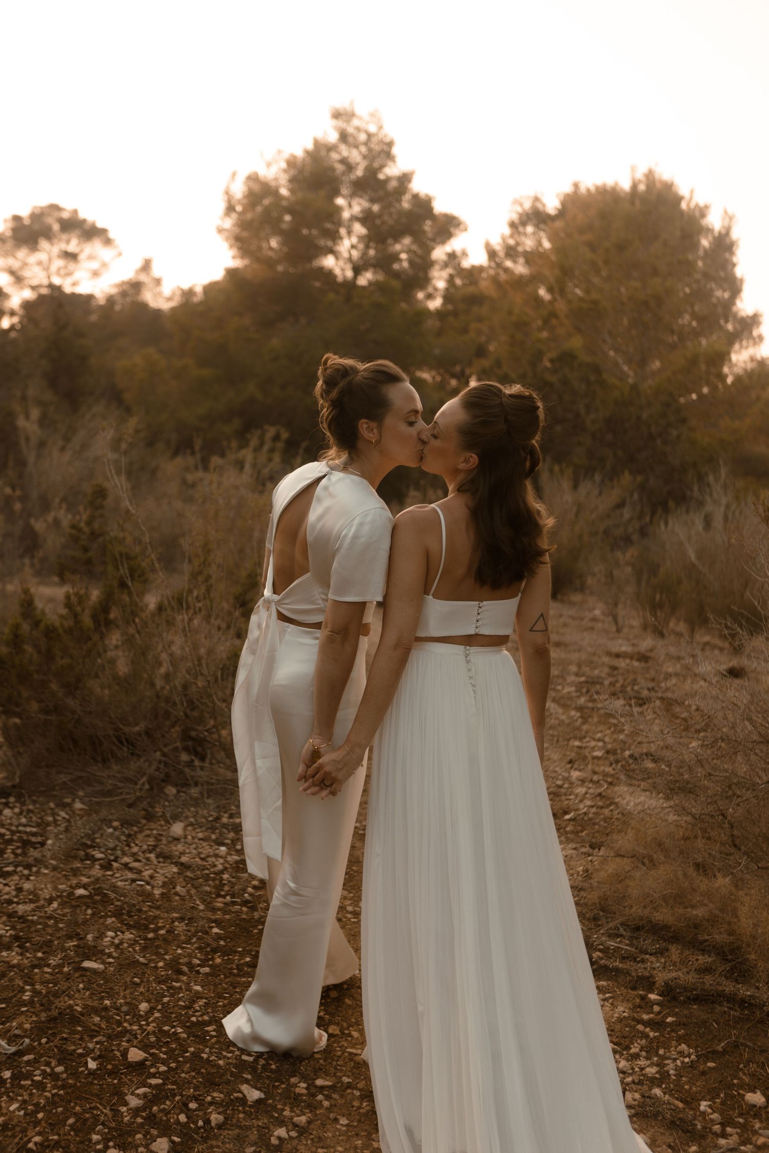 A romantic sunset photoshoot of a couple in matching white outfits standing on a dirt path.