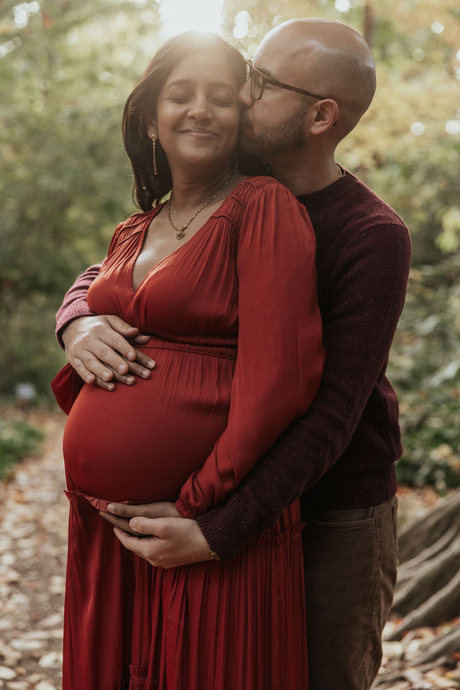 Intimate maternity photo of couple in autumn setting with red dress.