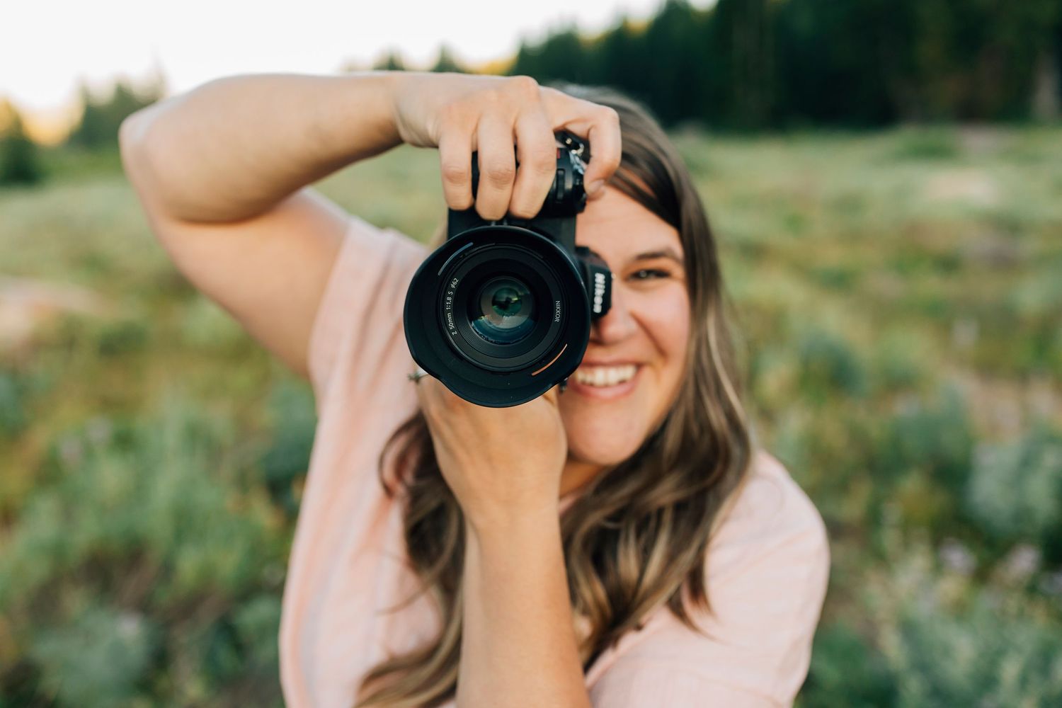 A photographer takes a photo with a professional camera in a meadow during golden hour.