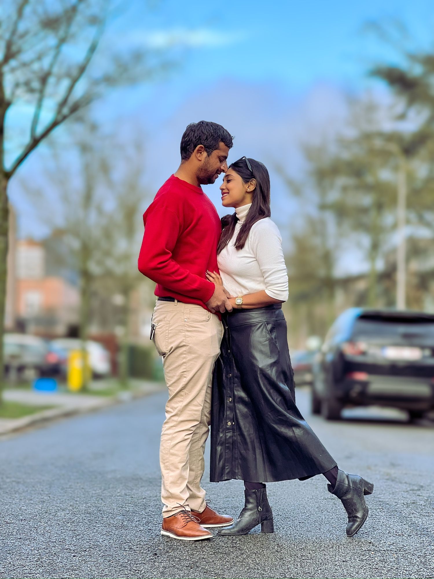 A couple in contrasting outfits share a romantic moment on a suburban street during a sunny day.