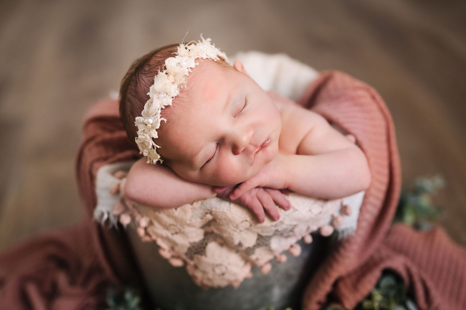Sleeping newborn with lace headband nestled in mauve blanket.