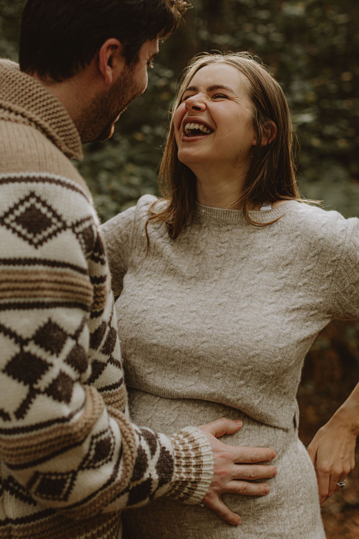 Couple in cozy sweaters laughing together during outdoor autumn photoshoot.