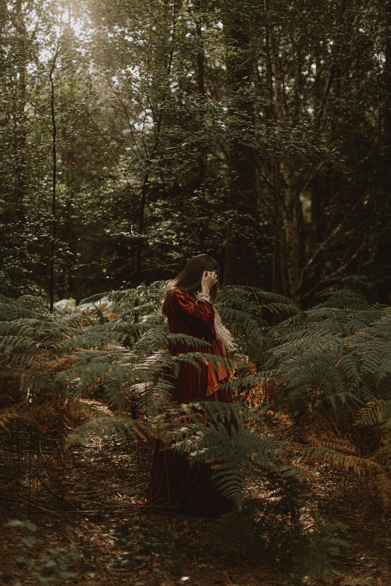 Figure in flowing red dress poses dramatically among woodland ferns.