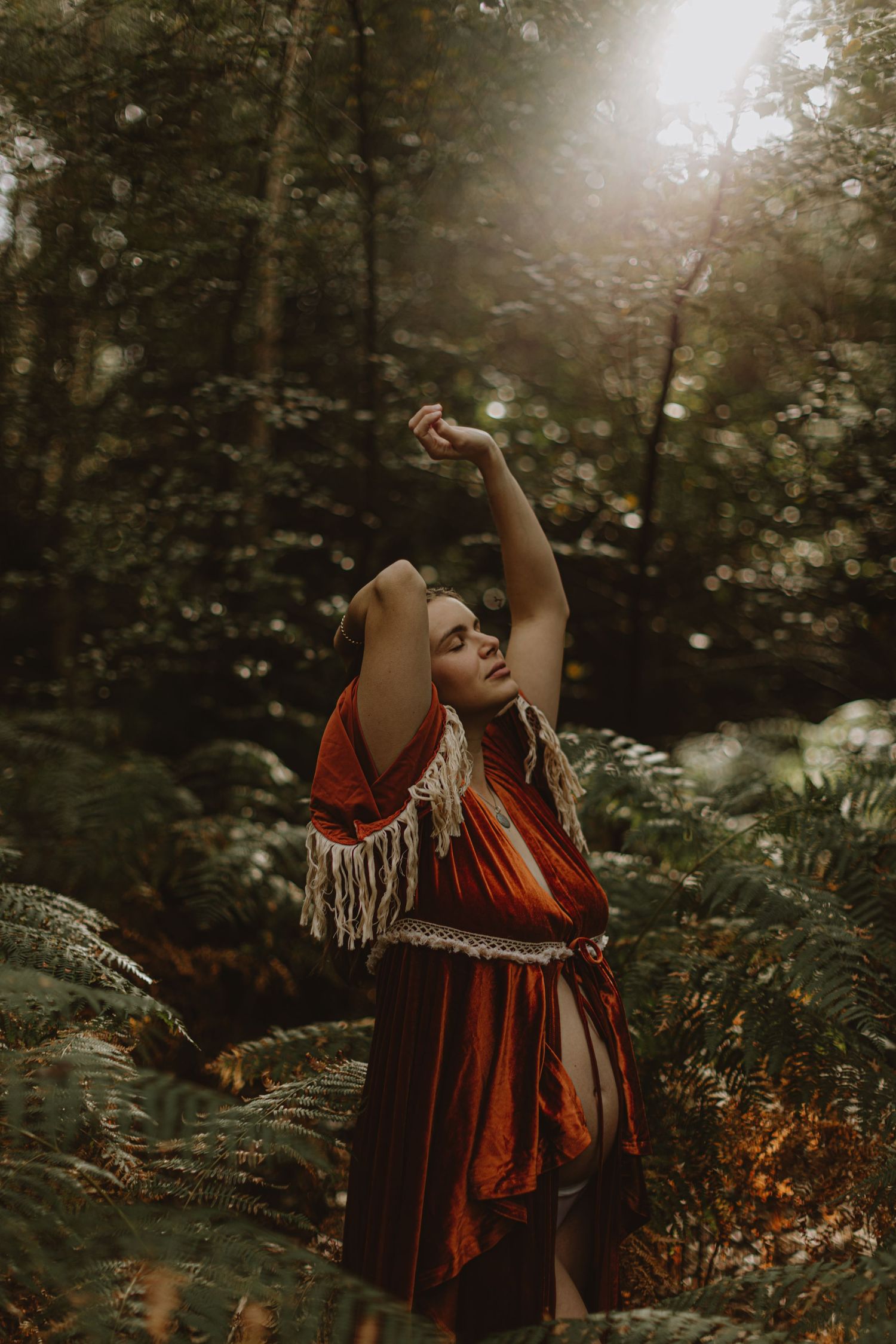 Person in red dress with fringe performs expressive dance movements in a forest.