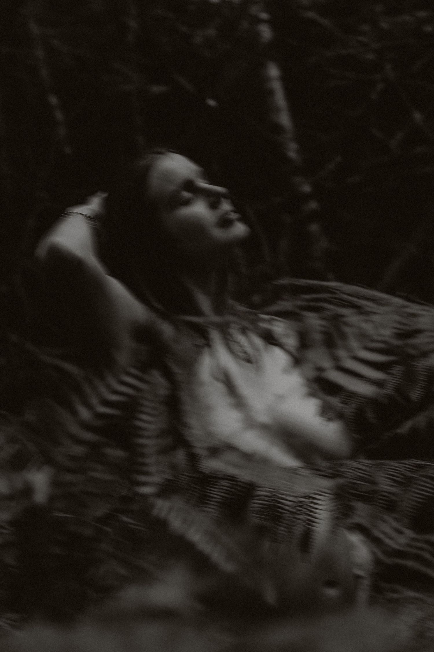 Artistic black and white portrait of a figure reclining in nature.