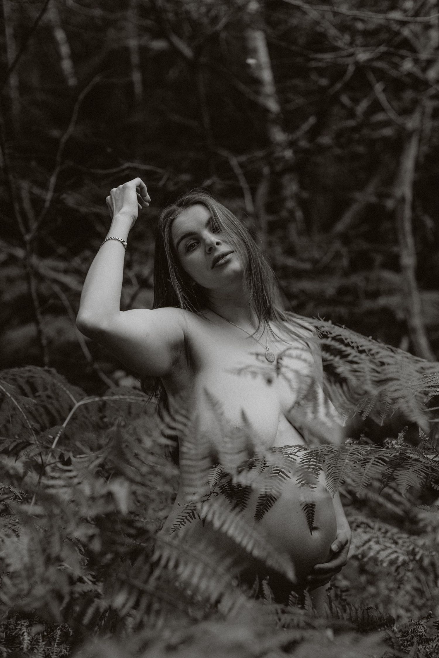Artistic black and white portrait amid ferns in dappled forest light.