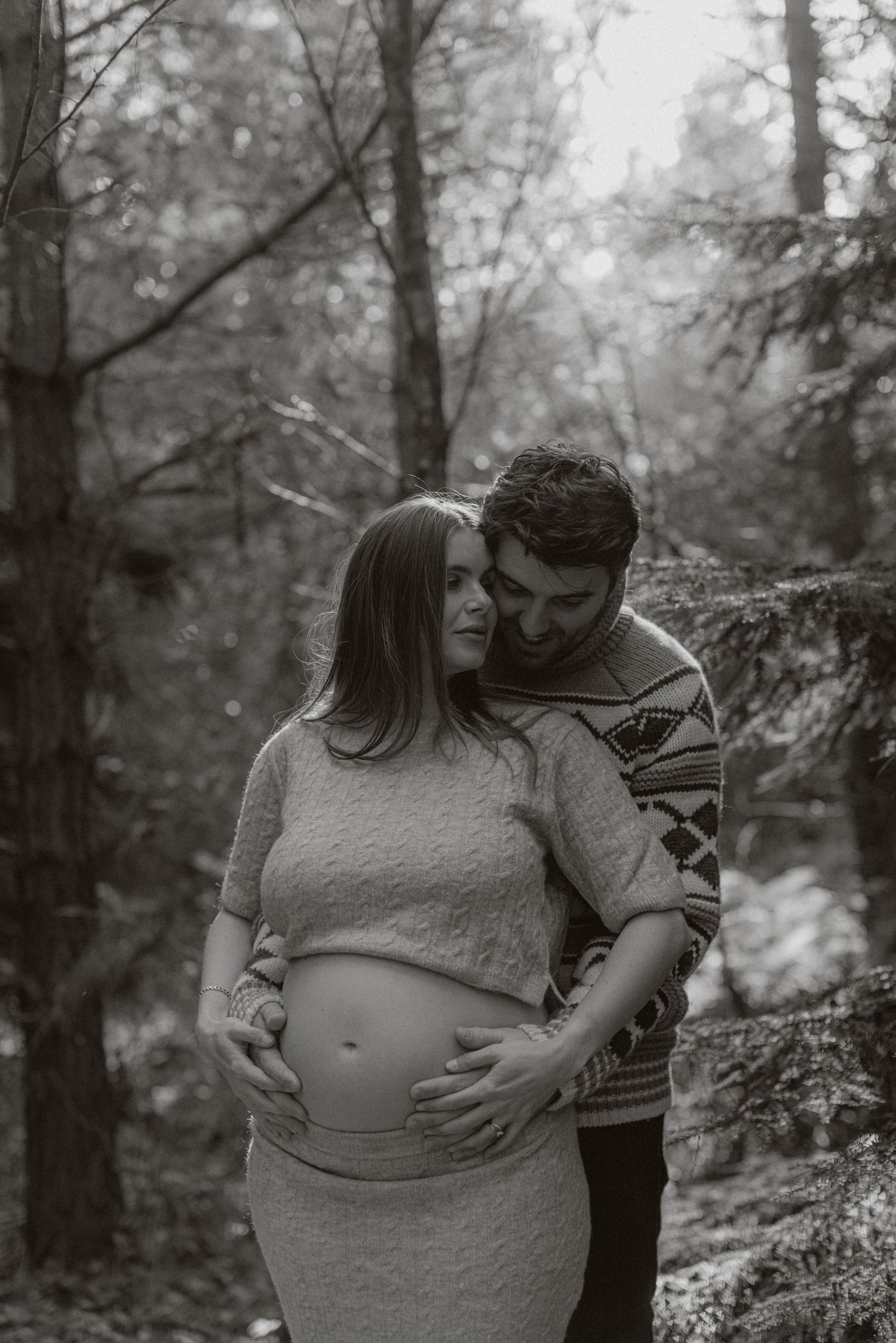 Intimate maternity moment captured in black and white forest setting.
