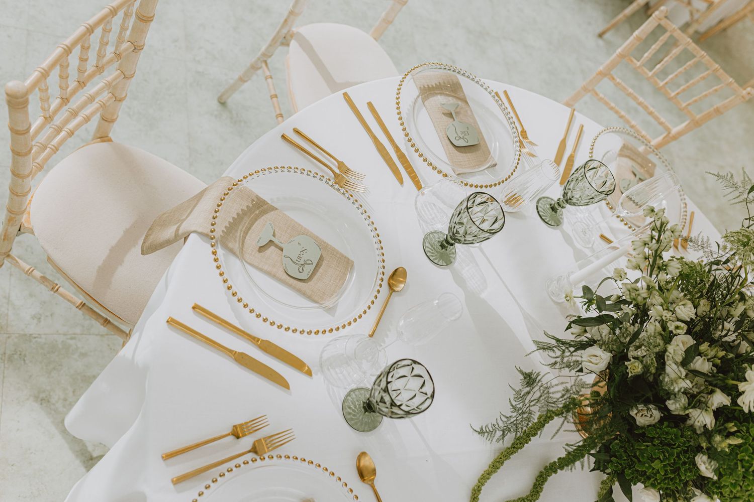 Elegant table setting with gold cutlery and white floral centerpieces at wedding reception.