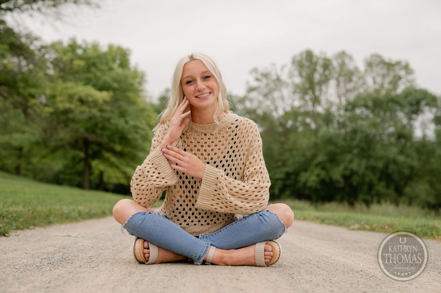 Natural lifestyle photo in crossed-leg pose on gravel path with bohemian sweater.