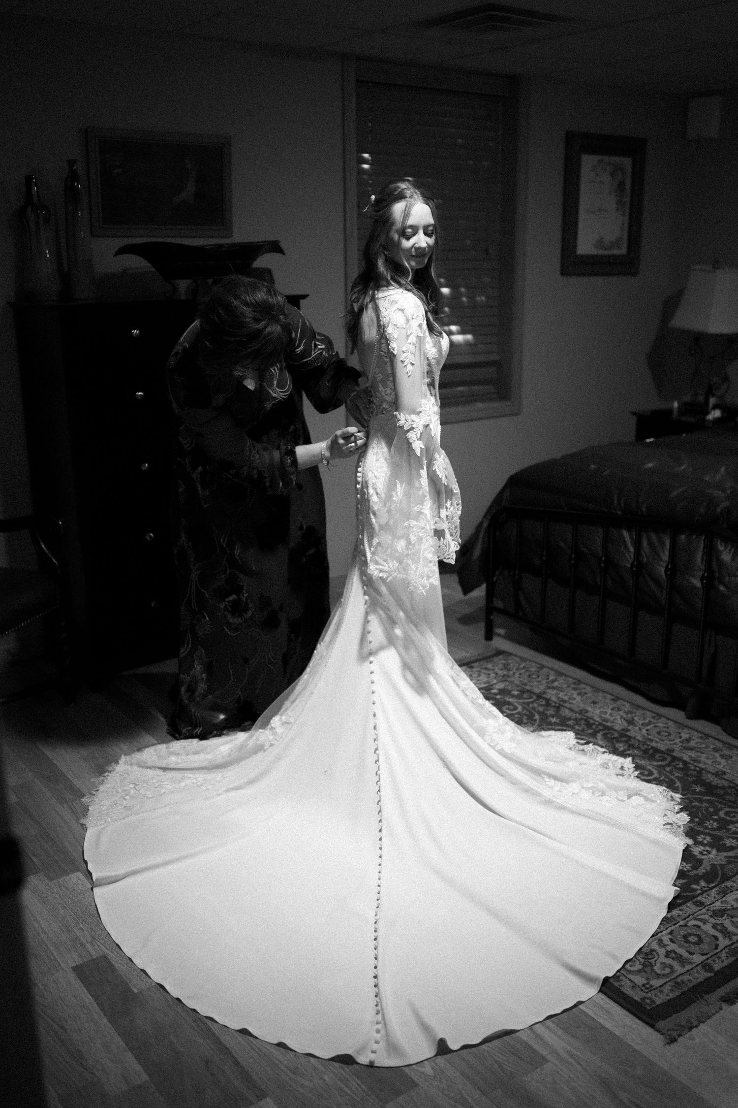 A dramatic black and white photo showcasing the long train of a lace wedding dress in an elegant bedroom.