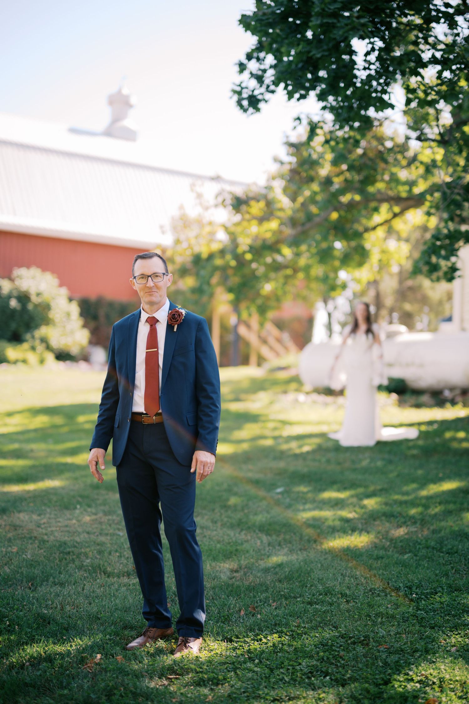 A formal wedding portrait taken outdoors with a red building and trees in the background.