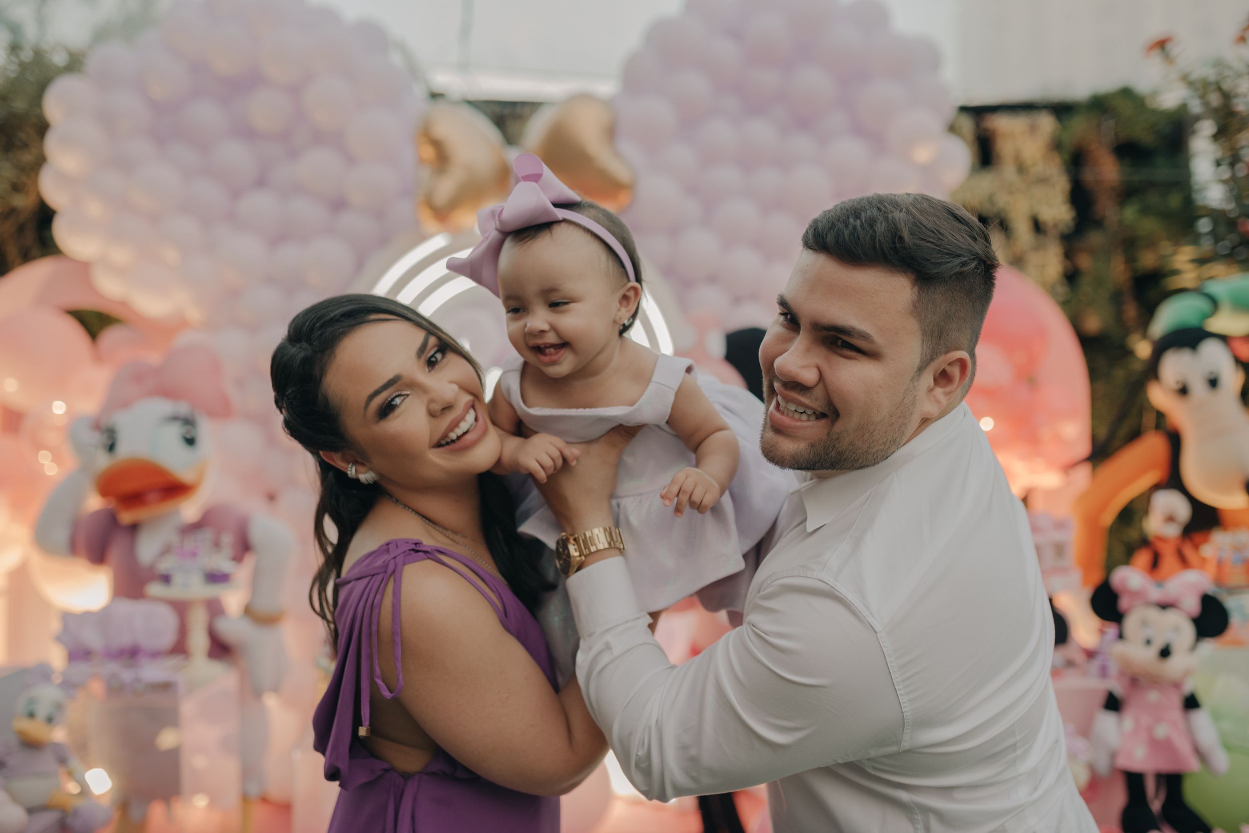 Happy family celebrating at party with Minnie Mouse themed decorations in background.