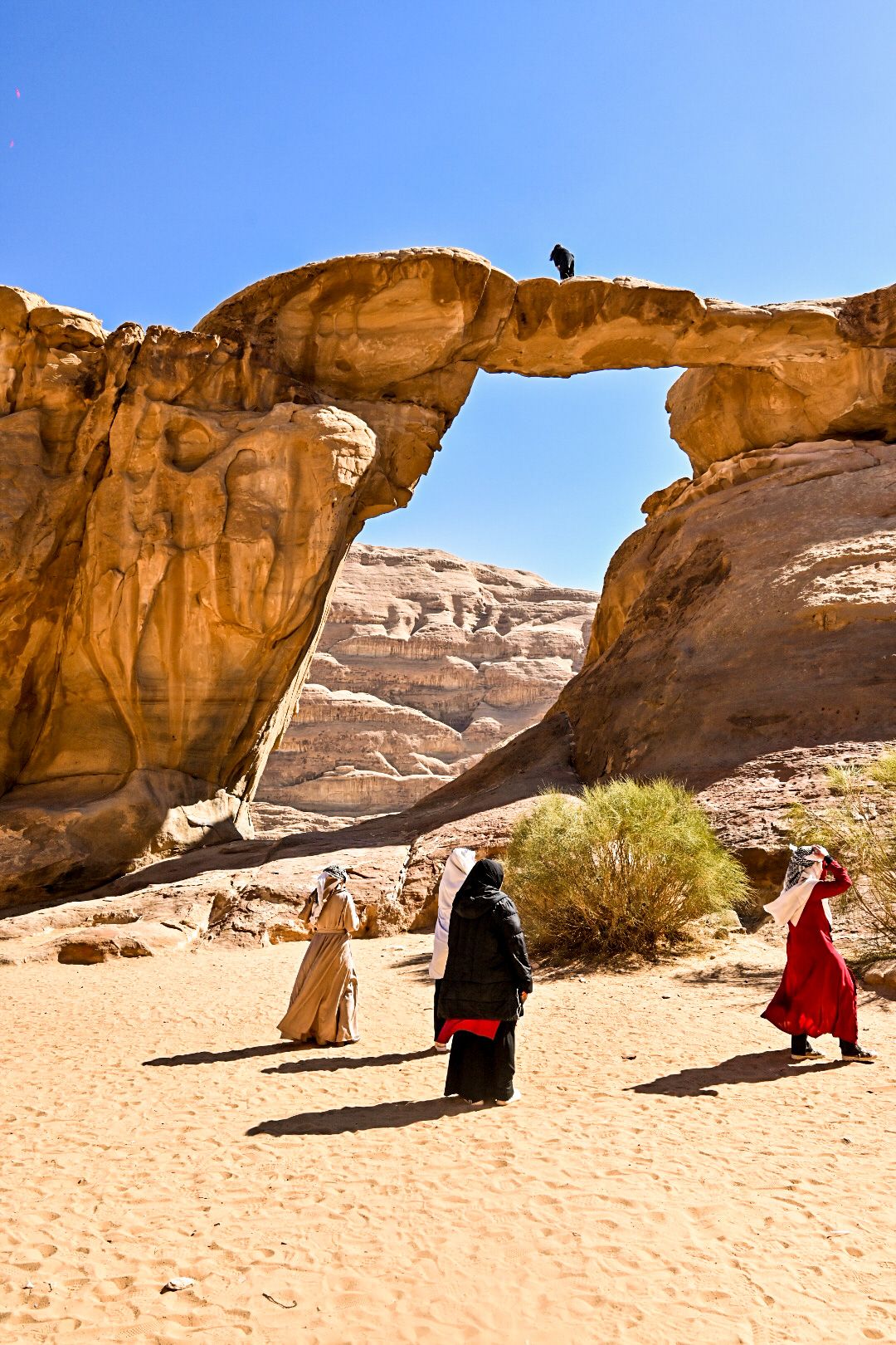 Natural rock arch formation in the desert with visitors admiring the massive stone structure.