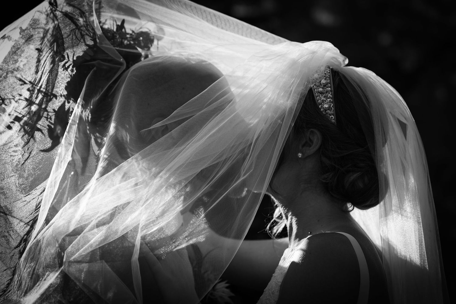 Black and white artistic photo of a bride's veil flowing in dramatic lighting.