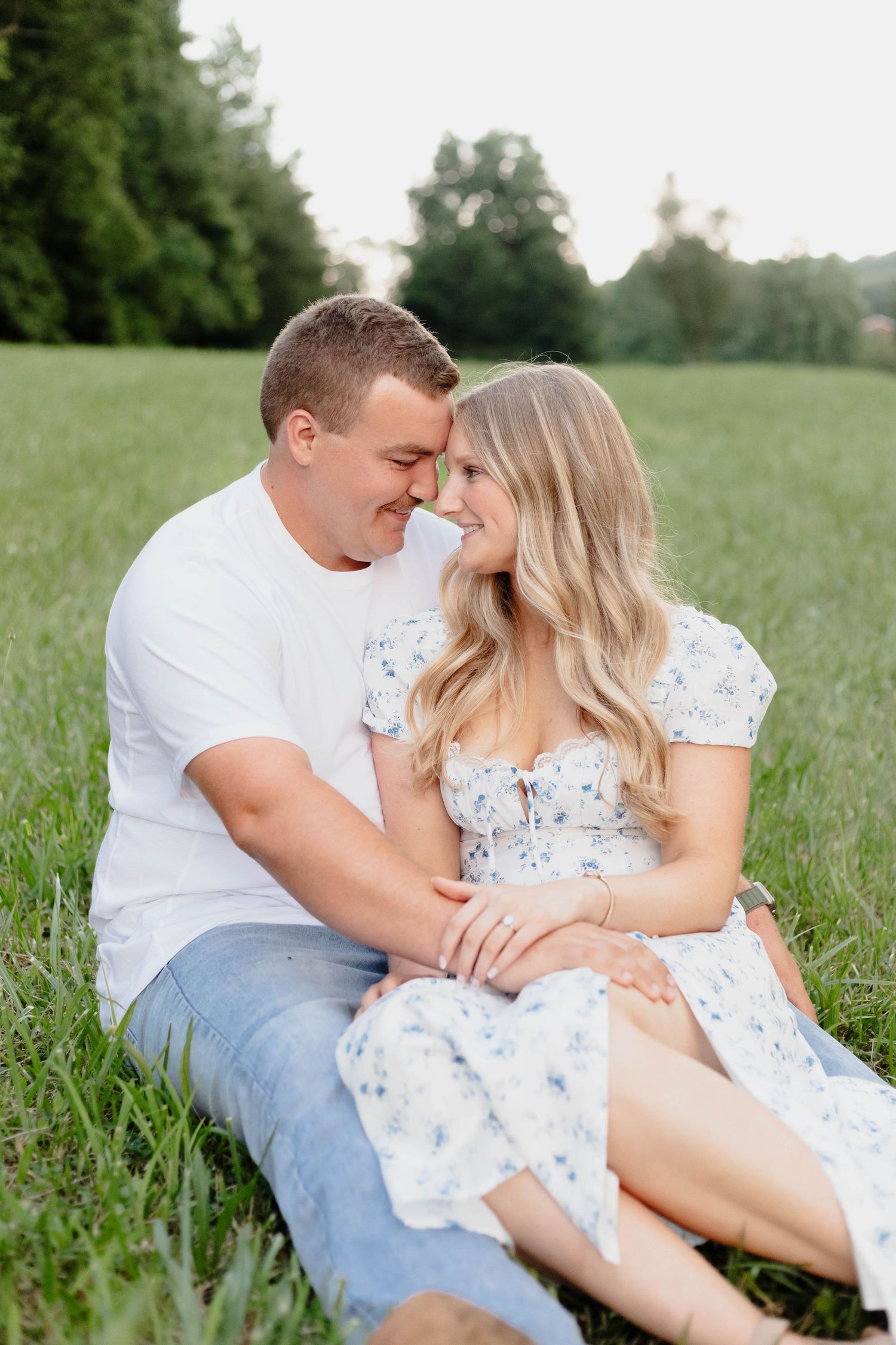 Romantic couple sitting together in a grassy meadow during a golden hour photoshoot.