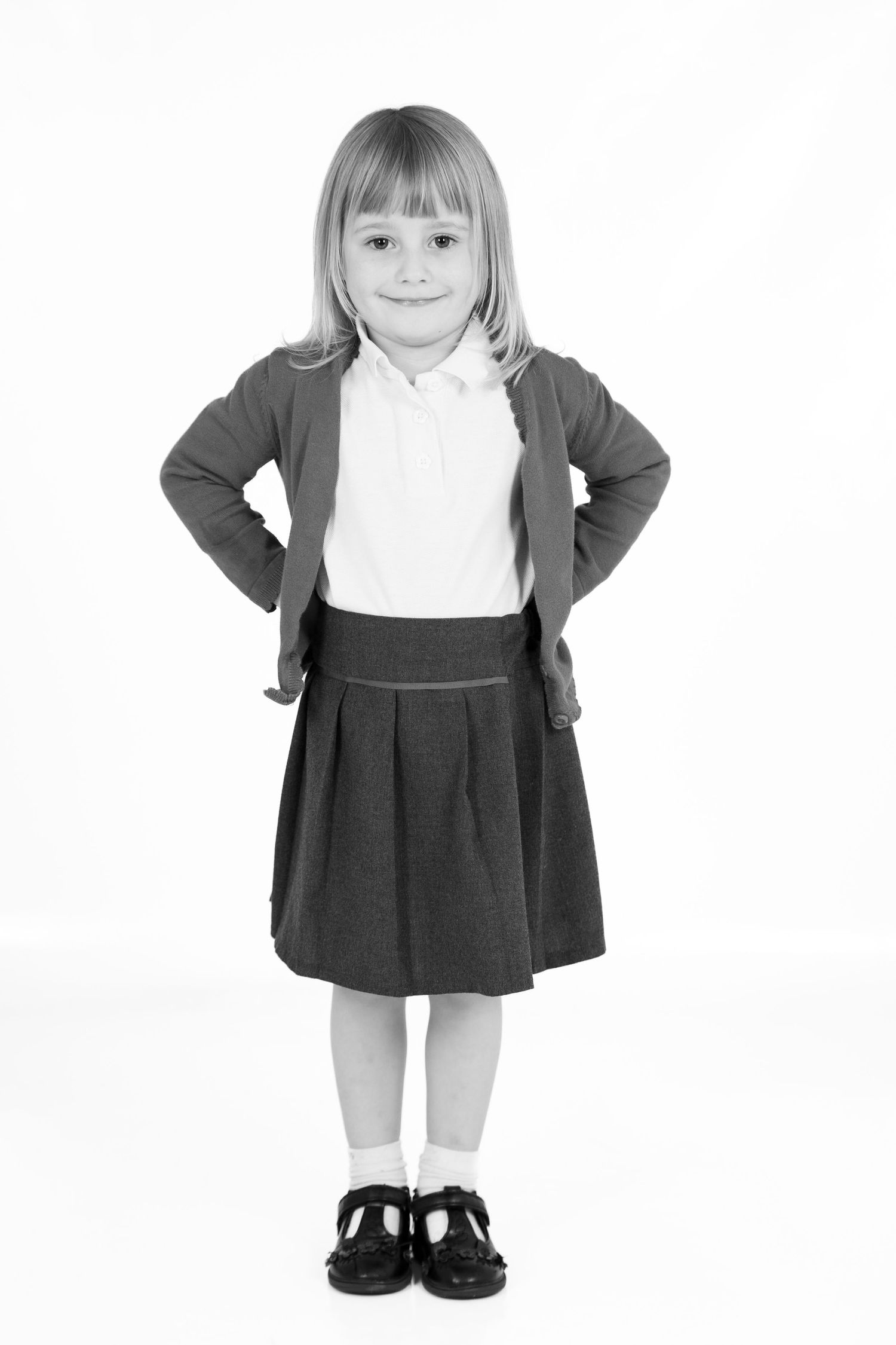 Young student in traditional school uniform poses with hands on hips against white background.