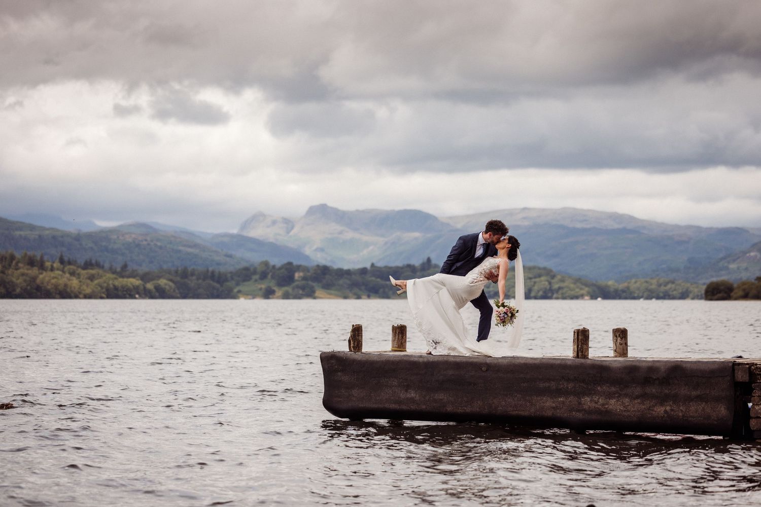 Groom kisses bride's head while she smiles - the backdrop is a country scene with cattle and it's raining