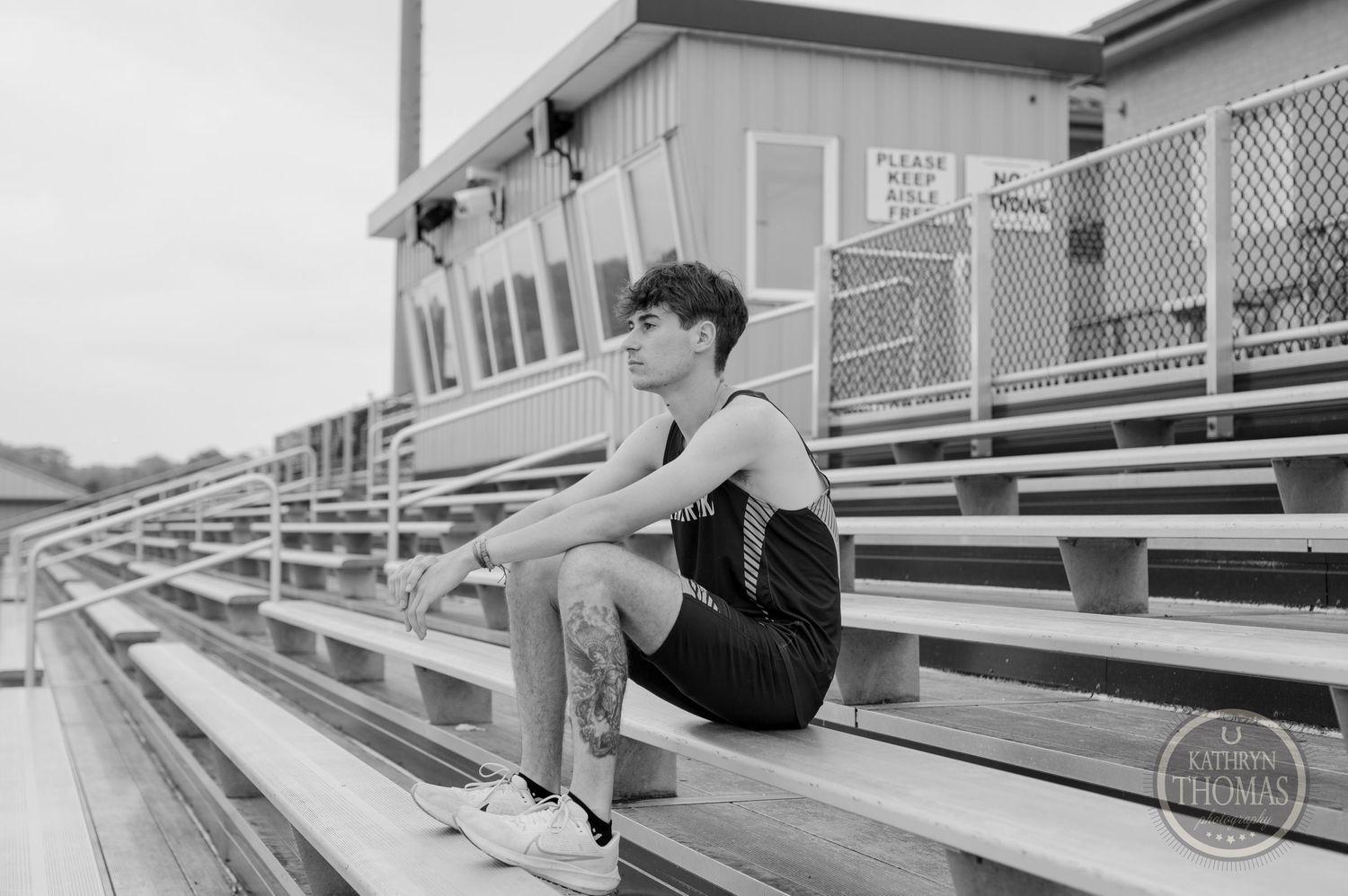 Black and white photo of athlete sitting on stadium bleachers.