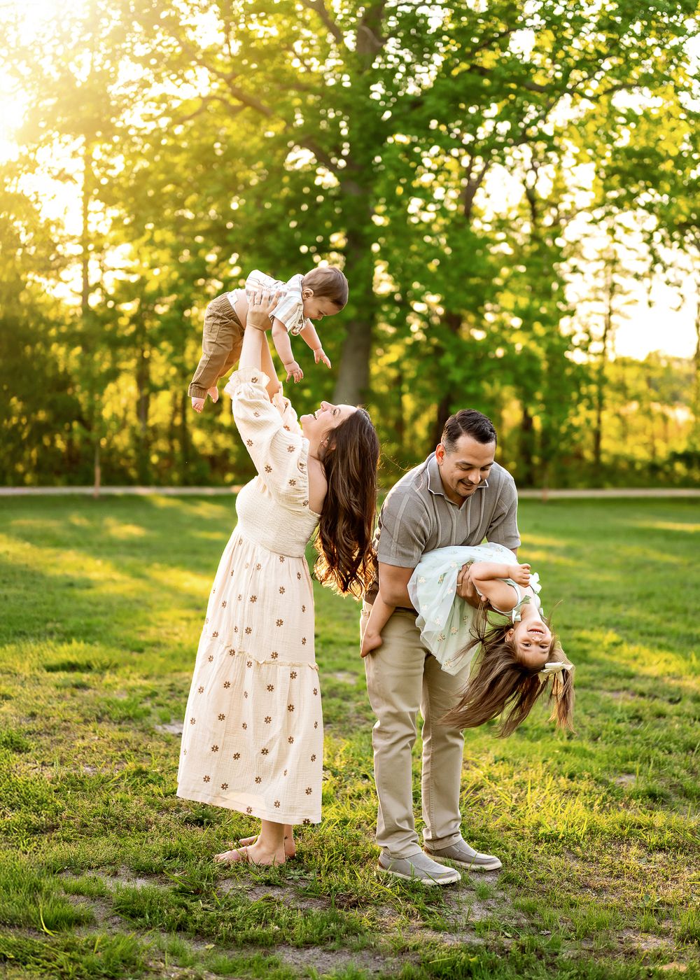 A family enjoys a playful moment together in a sun-dappled park during golden hour.