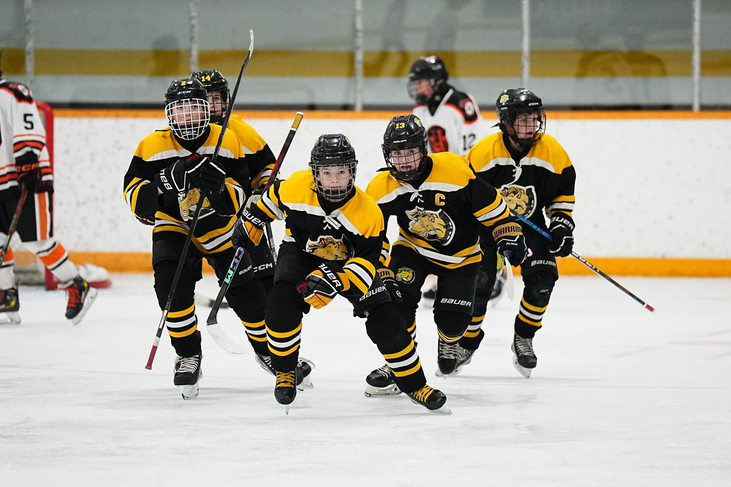 Young hockey players in black and yellow jerseys skate together on the ice during a youth hockey game.