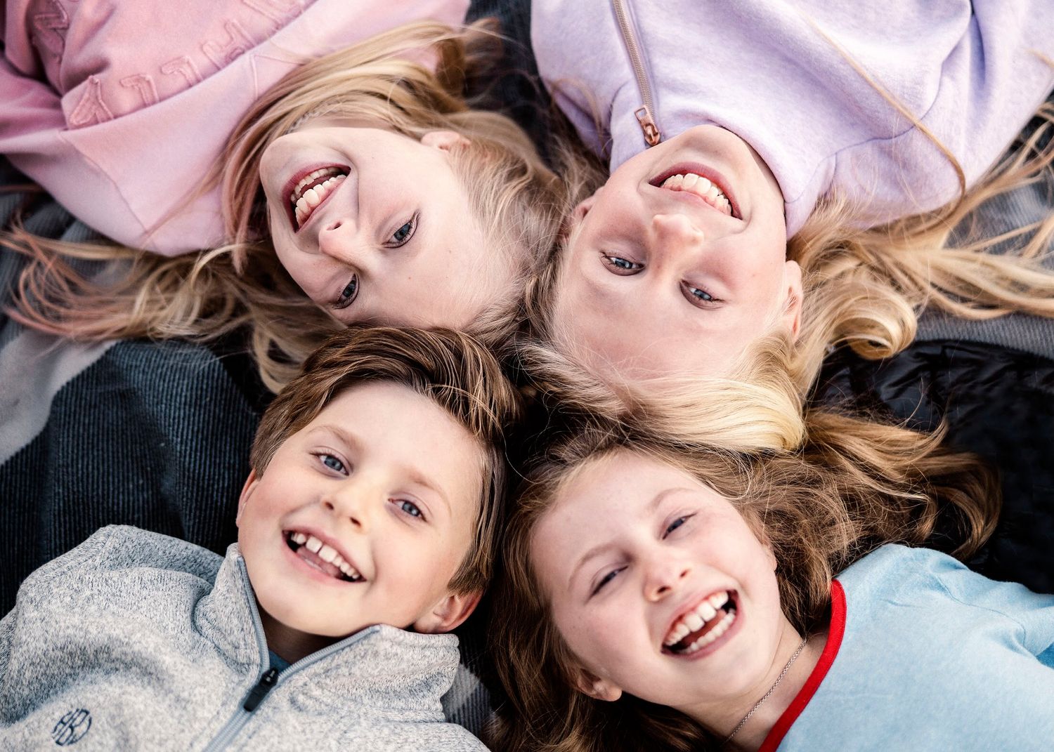 Children lying on ground with hair spread out in circular formation during photoshoot.