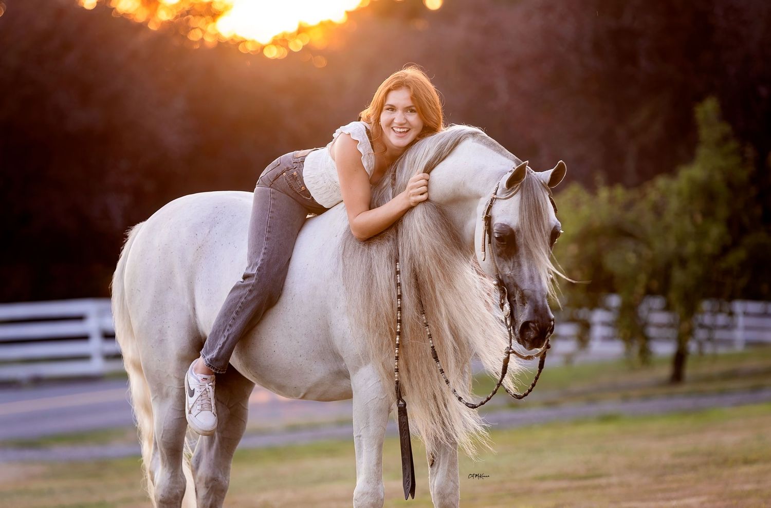 Teenage girl laying on her grey Arabian stallion's neck at sunset