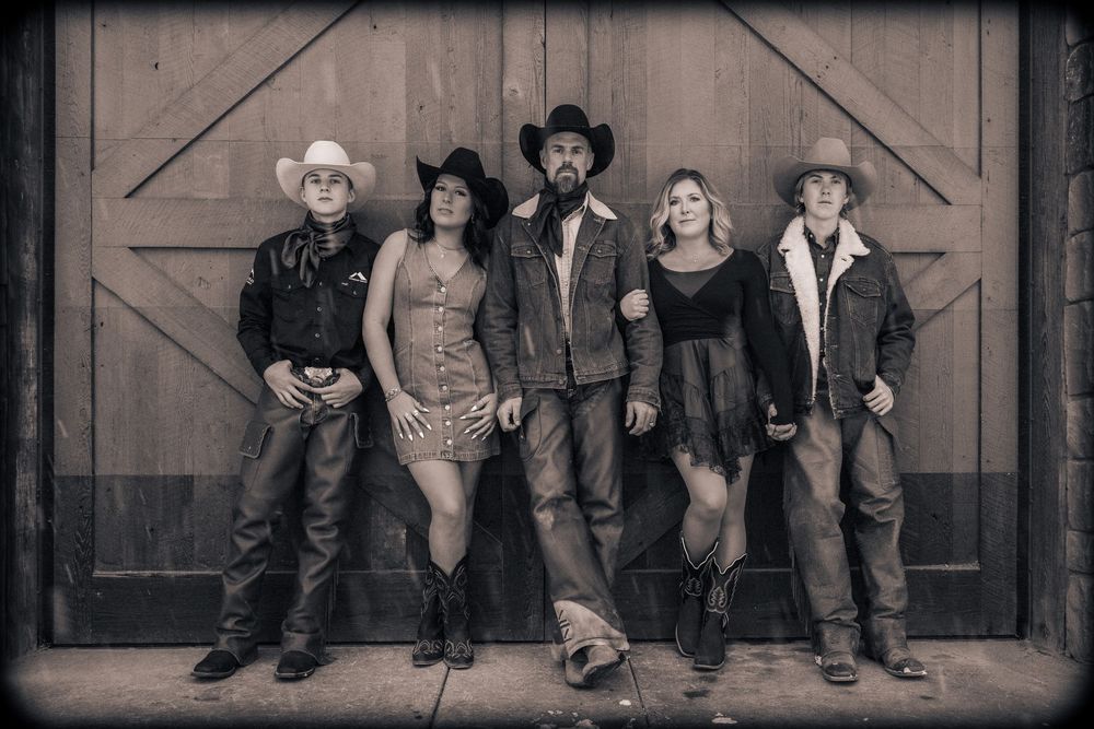 Four people sit casually on wooden steps in rustic western attire with cowboy hats and boots.