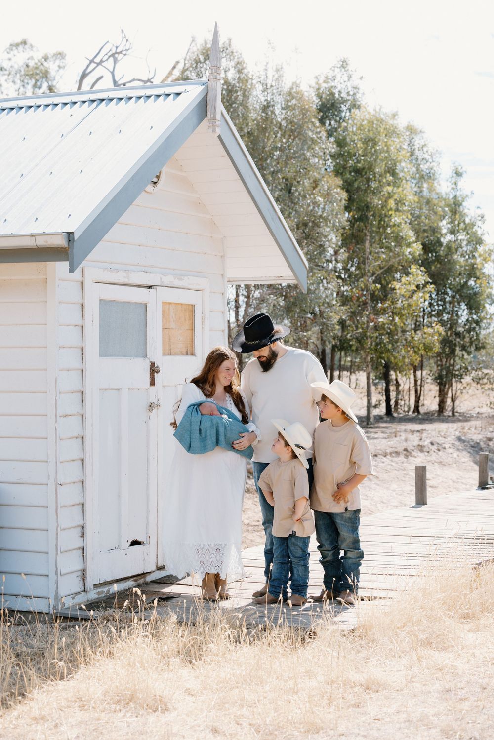 Rustic white wooden cabins stand in a row against a rural landscape with dry grass and trees.