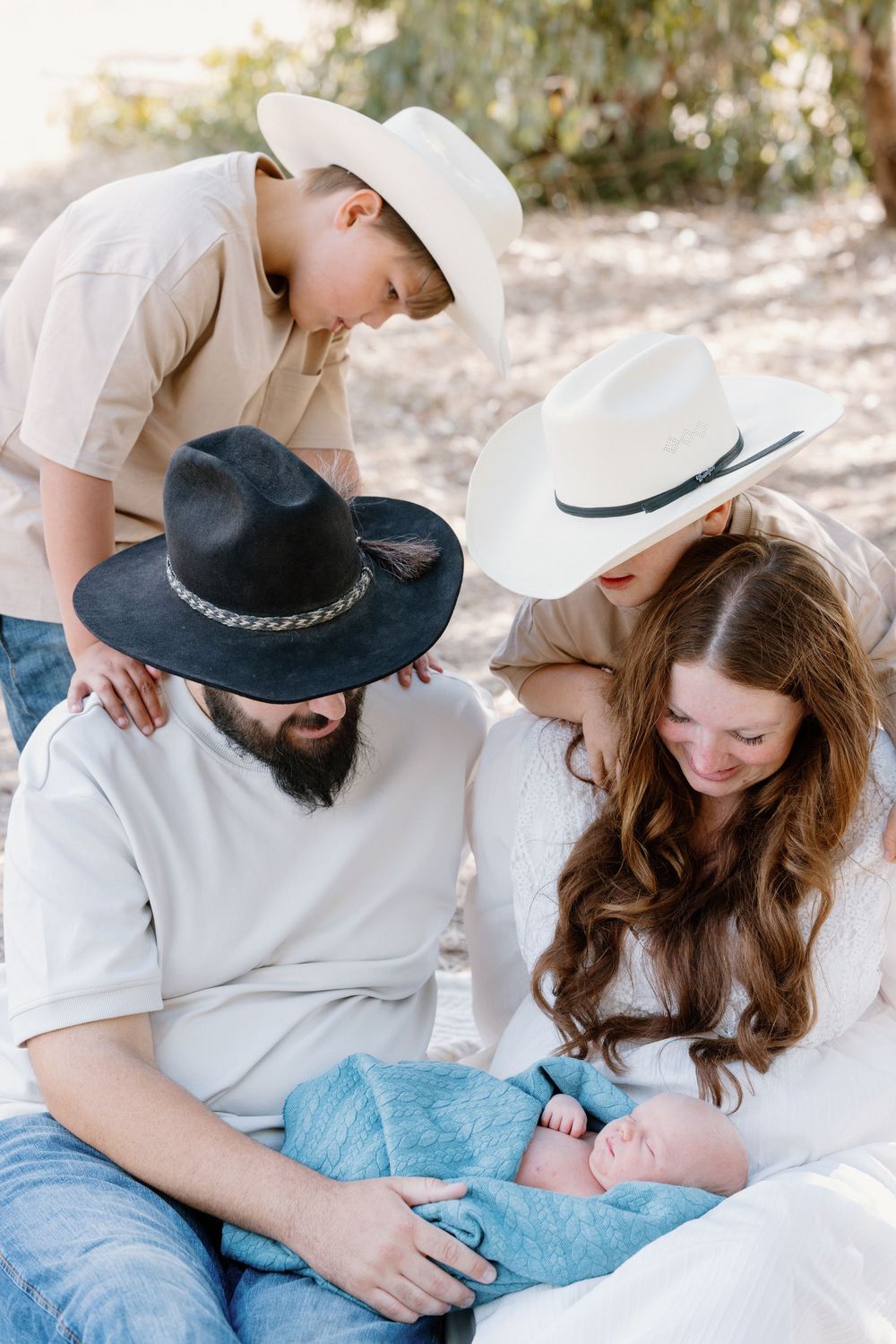 A couple in cowboy hats share an intimate moment outdoors in casual western attire.