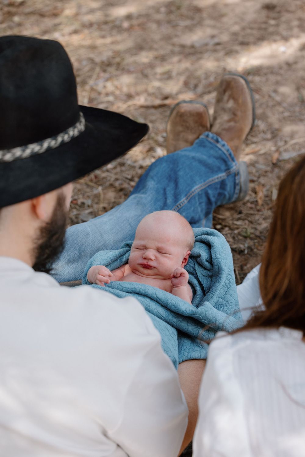 A sleeping newborn baby wrapped in blue blanket being held by parents.