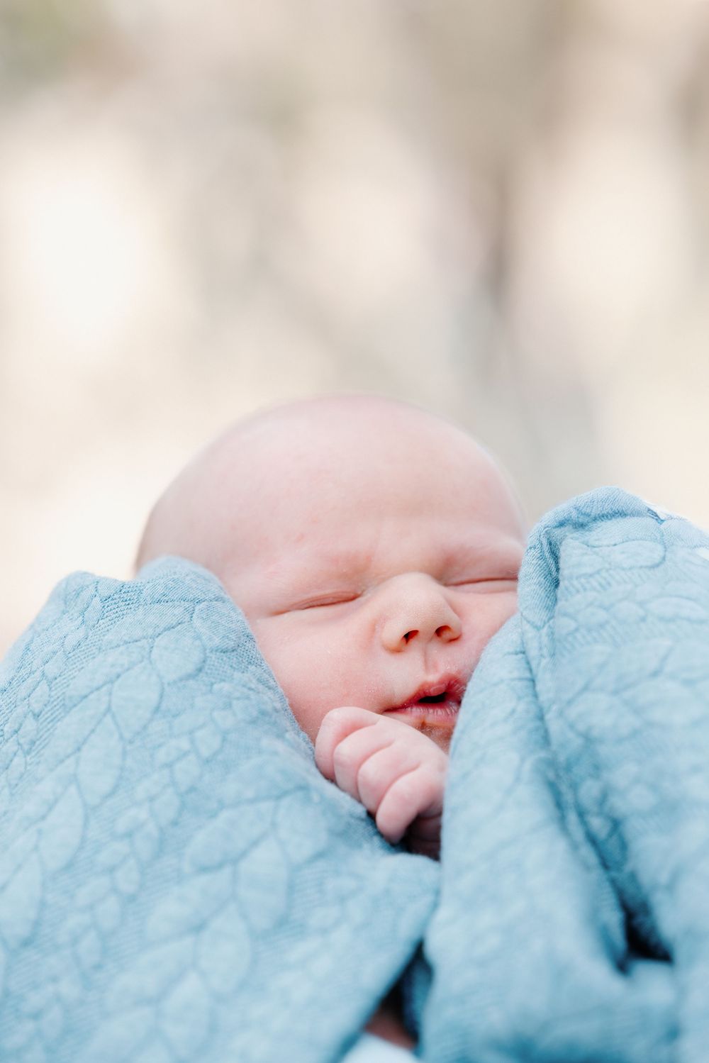 Close-up of a peaceful sleeping baby wrapped in soft blue textured blanket.