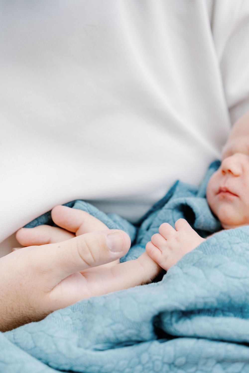 Gentle hands tenderly hold a soft turquoise blanket against white fabric in a series of intimate close-up shots.