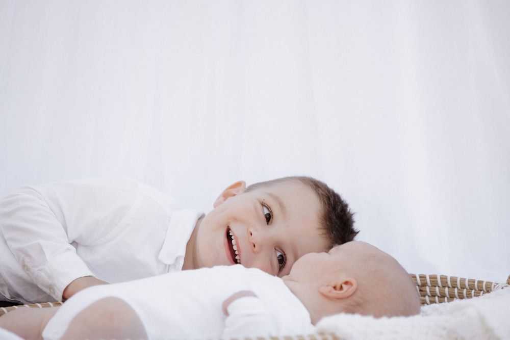 Two young children lying together on white bedding, sharing a sweet bonding moment. location shepparton