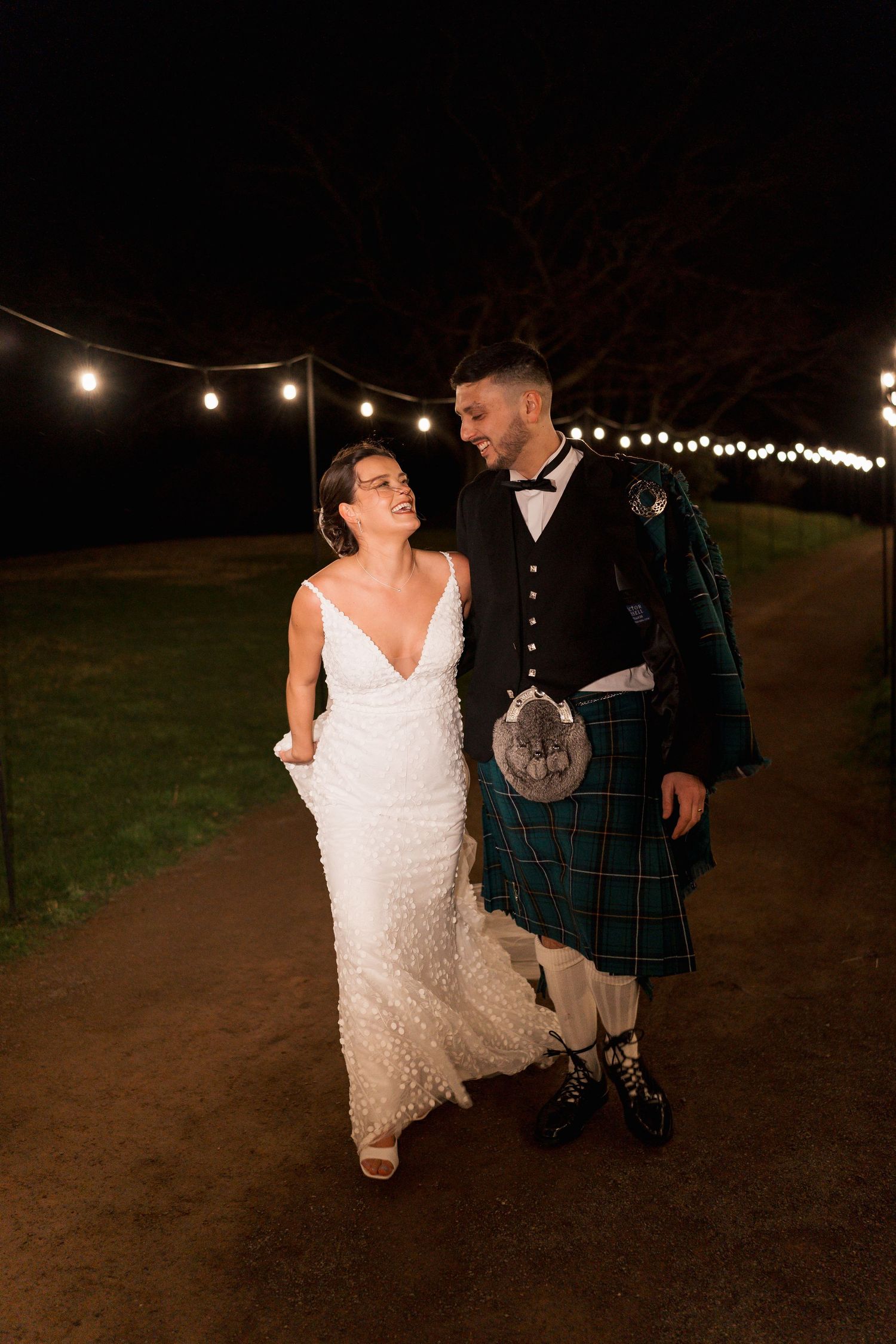 N&C walking along a lit path. Natural candid wedding photography.